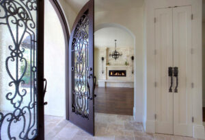 Arched wrought iron entry door with decorative glass opening into a bright luxury home interior with stone fireplace