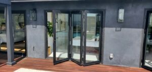 Black framed folding glass patio door partially open to sunlit deck